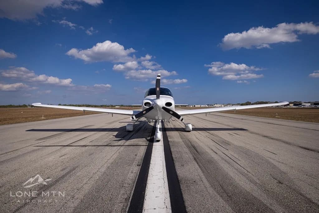 A head-on view of the white N186SB single-engine aircraft with its propeller, centered on a runway.
