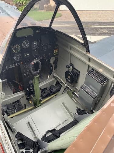 The cockpit of a P-40 Warhawk replica aircraft showing the instrument panel and controls.
