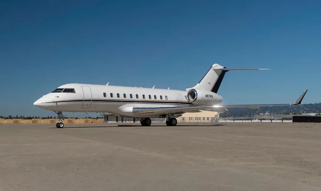 A white Bombardier Global 6000 private jet with black and gold accents on the tail, registration N878HL, parked on an tarmac under a clear blue sky.