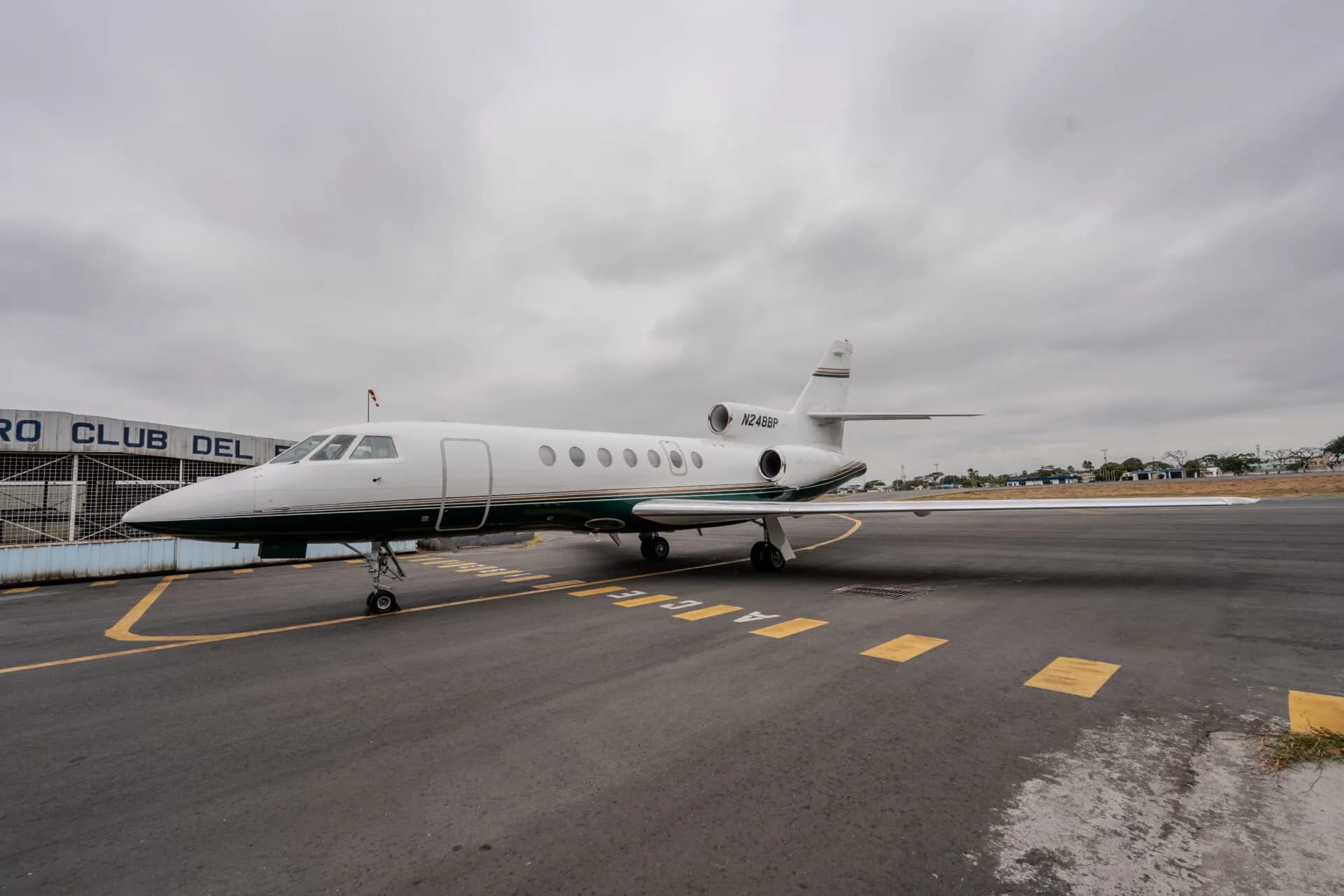 A white and green private jet (N248BP) parked on an airfield under a cloudy sky.