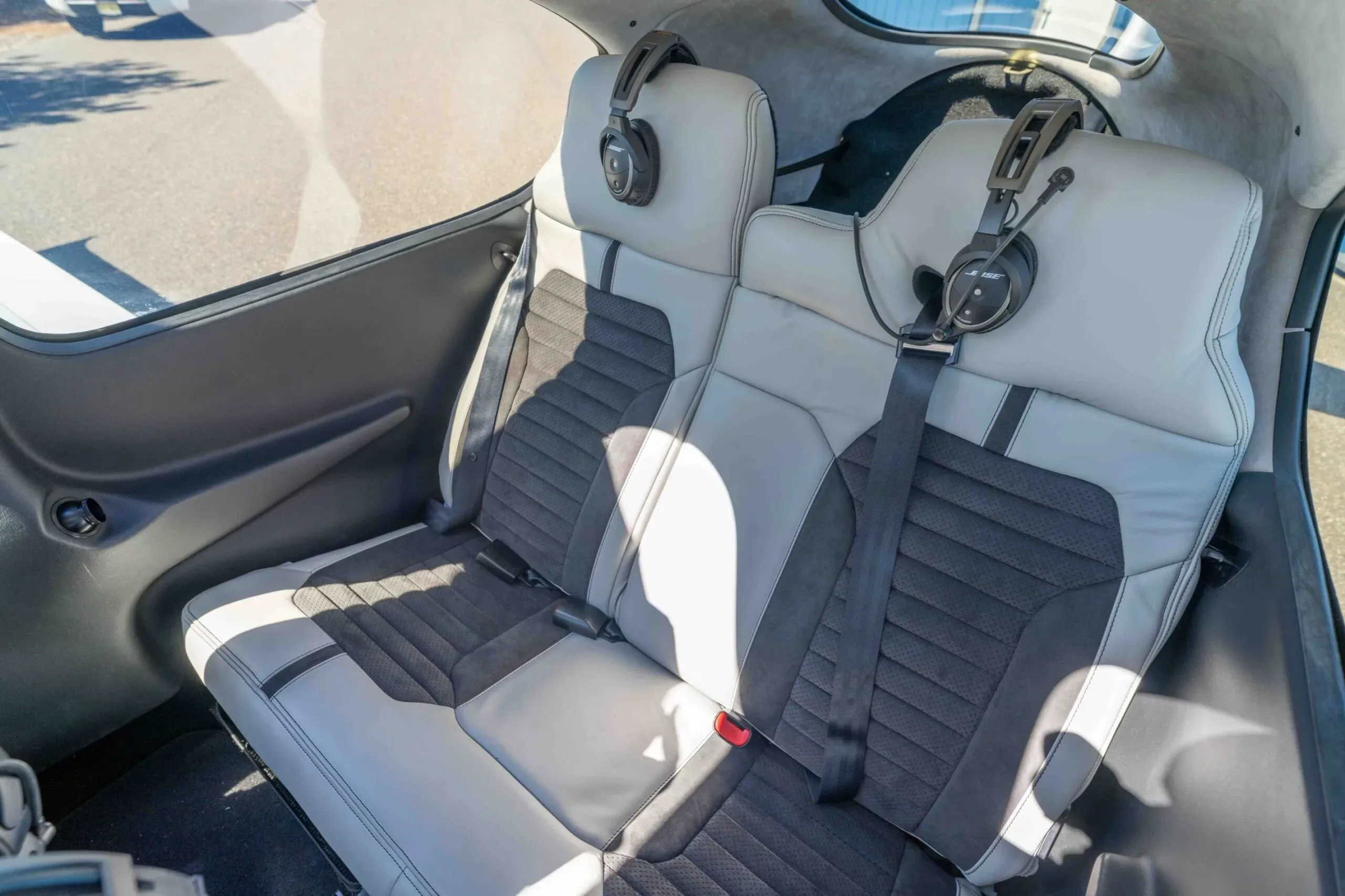 An angled view of the light gray and dark gray two-tone rear passenger seats of the aircraft, with two headsets.