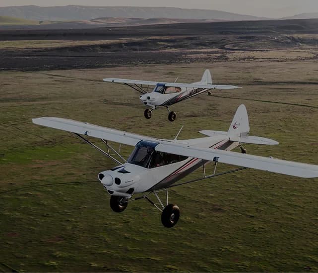 Two white and gray aircraft flying over a green field.