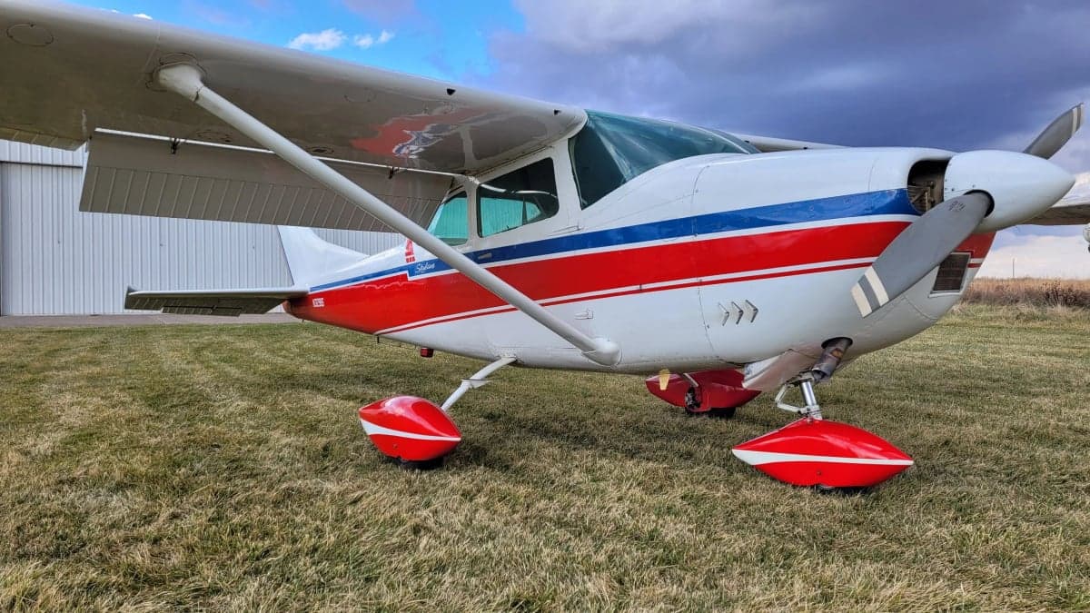A low angle view of the Cessna Skylane with red, white, and blue paint scheme on a grassy field.