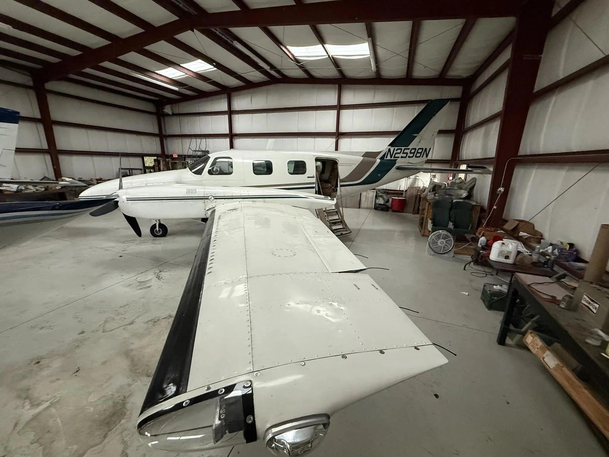 A white twin-engine Piper Navajo aircraft with green and brown stripes, seen from above the right wing in a hangar.