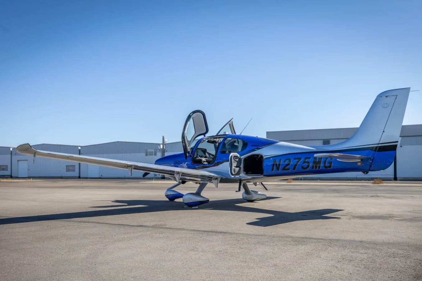 A side view of the blue and silver Cirrus SR22 aircraft, N275MG, with its doors open on the tarmac.