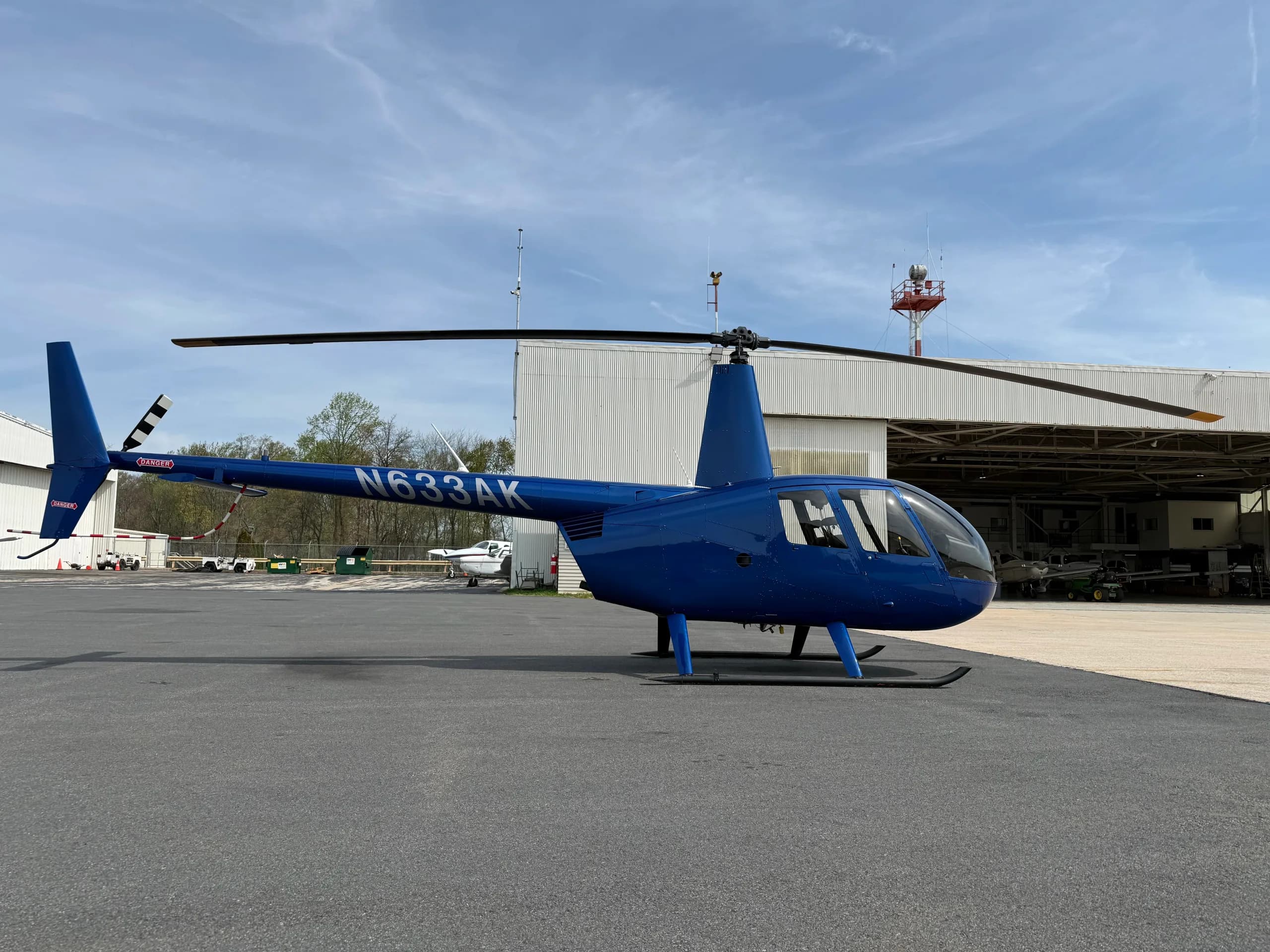 A blue Robinson R44 helicopter, N633AK, parked on an asphalt tarmac next to a white hangar.