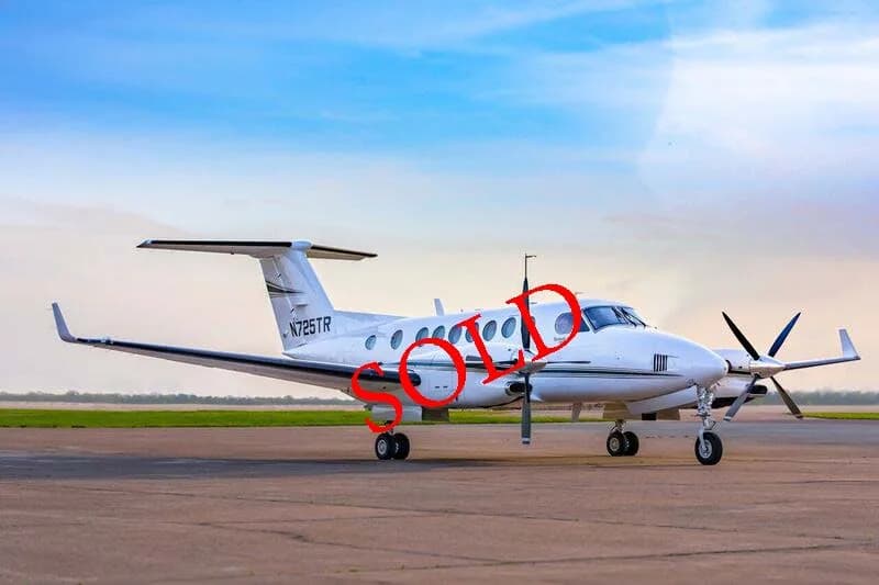 A white Beechcraft King Air 350i with tail number N725TR is parked on an airfield under a blue sky.