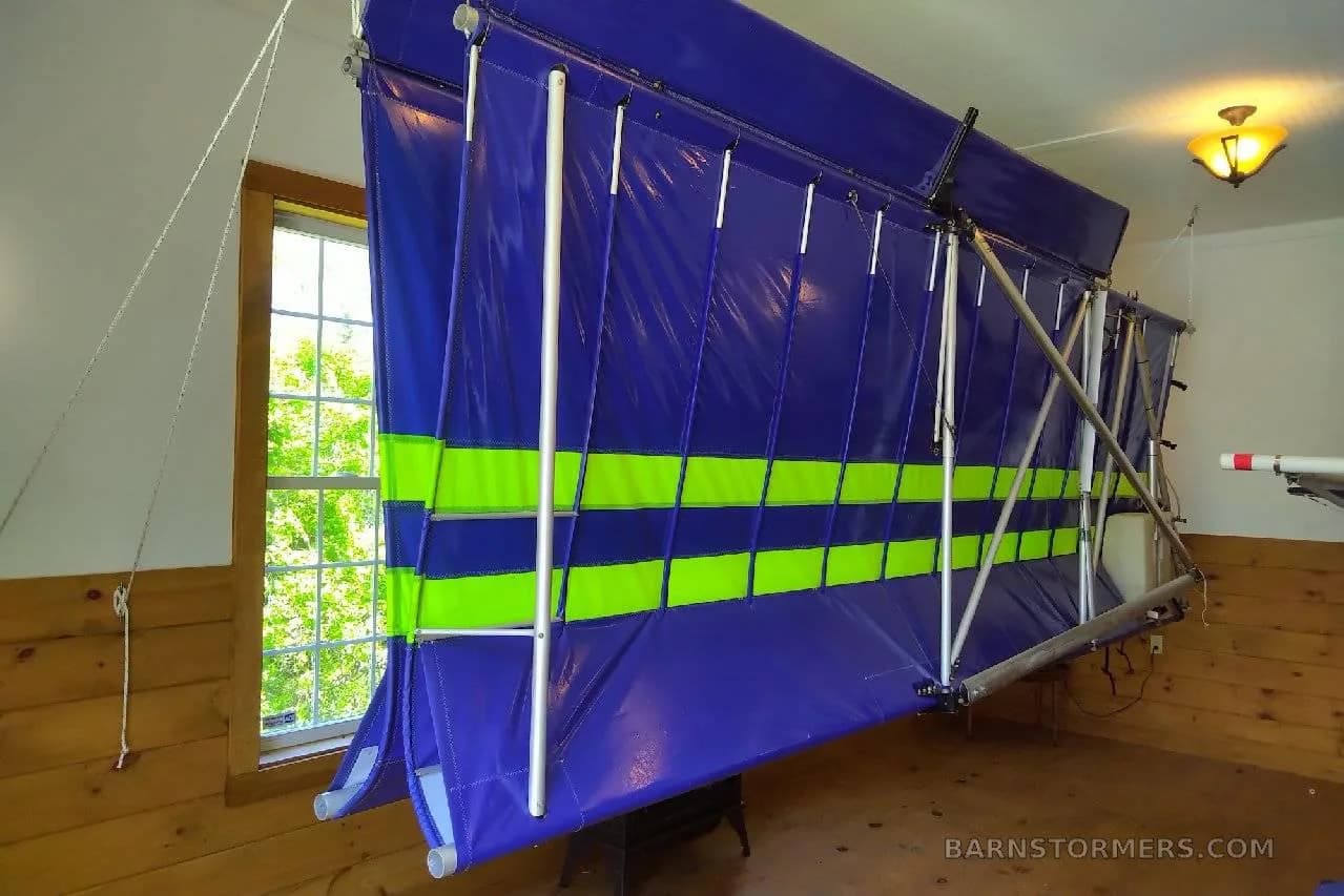 A large blue fabric wing with green stripes, likely from an ultralight aircraft, stored indoors.