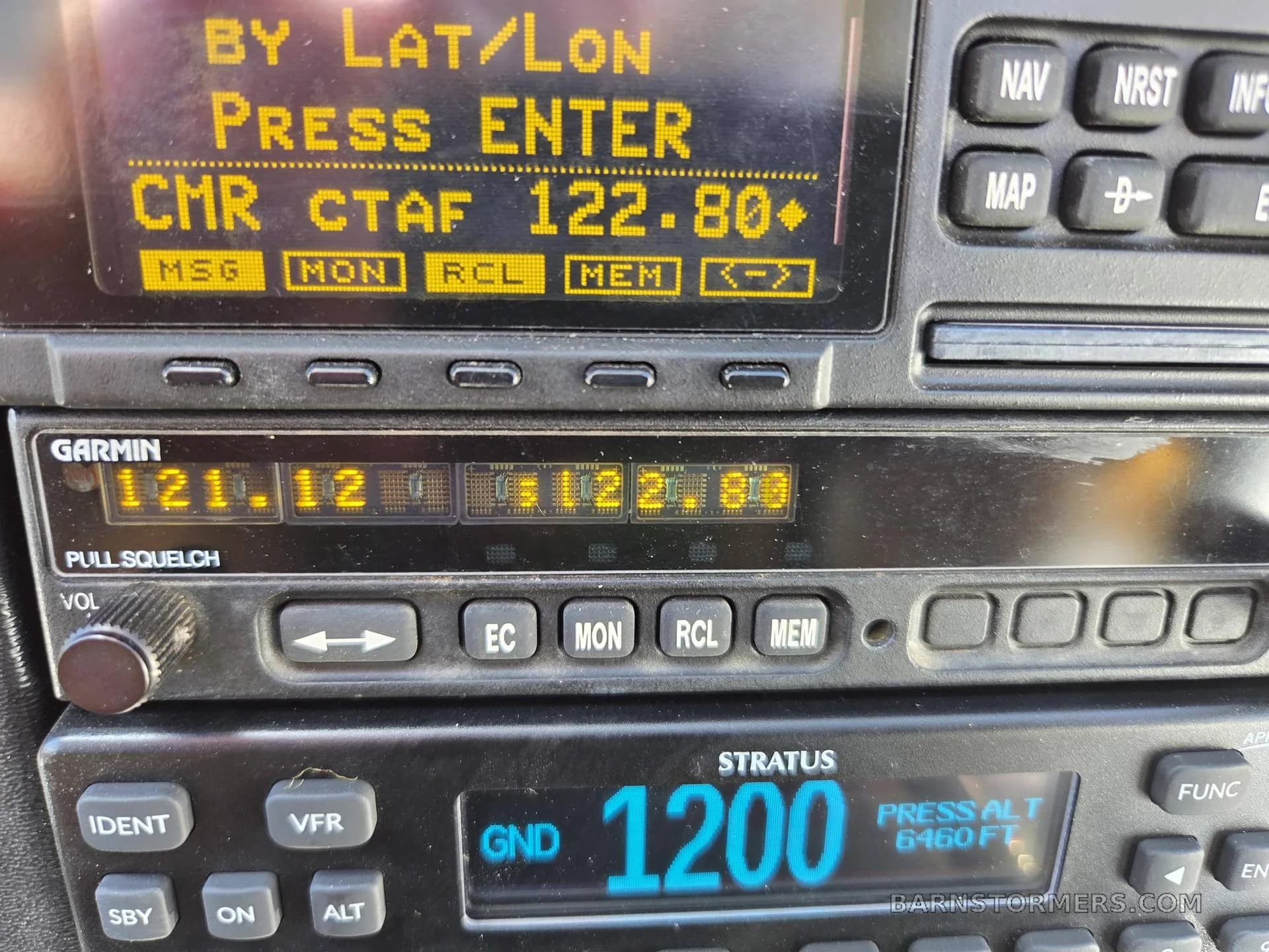 A detailed close-up of the Garmin and Stratus avionics units in an aircraft cockpit, displaying frequencies and altitude.