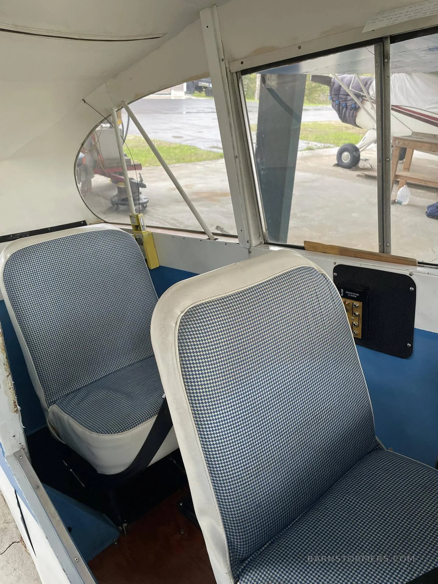 The interior cabin of a light aircraft, showing two seats upholstered in a blue and white houndstooth pattern.