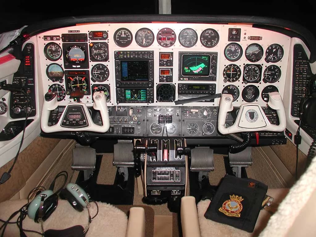 The aircraft cockpit features a complex instrument panel with analog gauges, digital displays, two control yokes, and throttle quadrant.