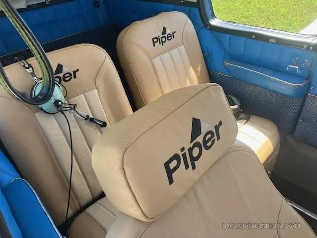 Tan leather aircraft seats with the 'Piper' logo are visible in the blue-paneled cabin.