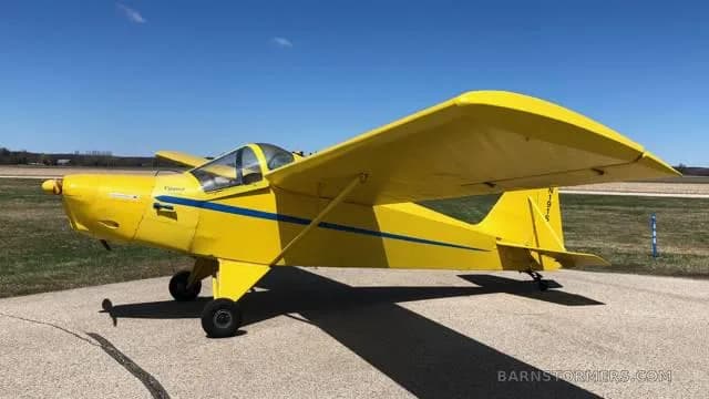 A bright yellow single-engine experimental aircraft with blue stripes, viewed from the right side, parked on an asphalt surface.