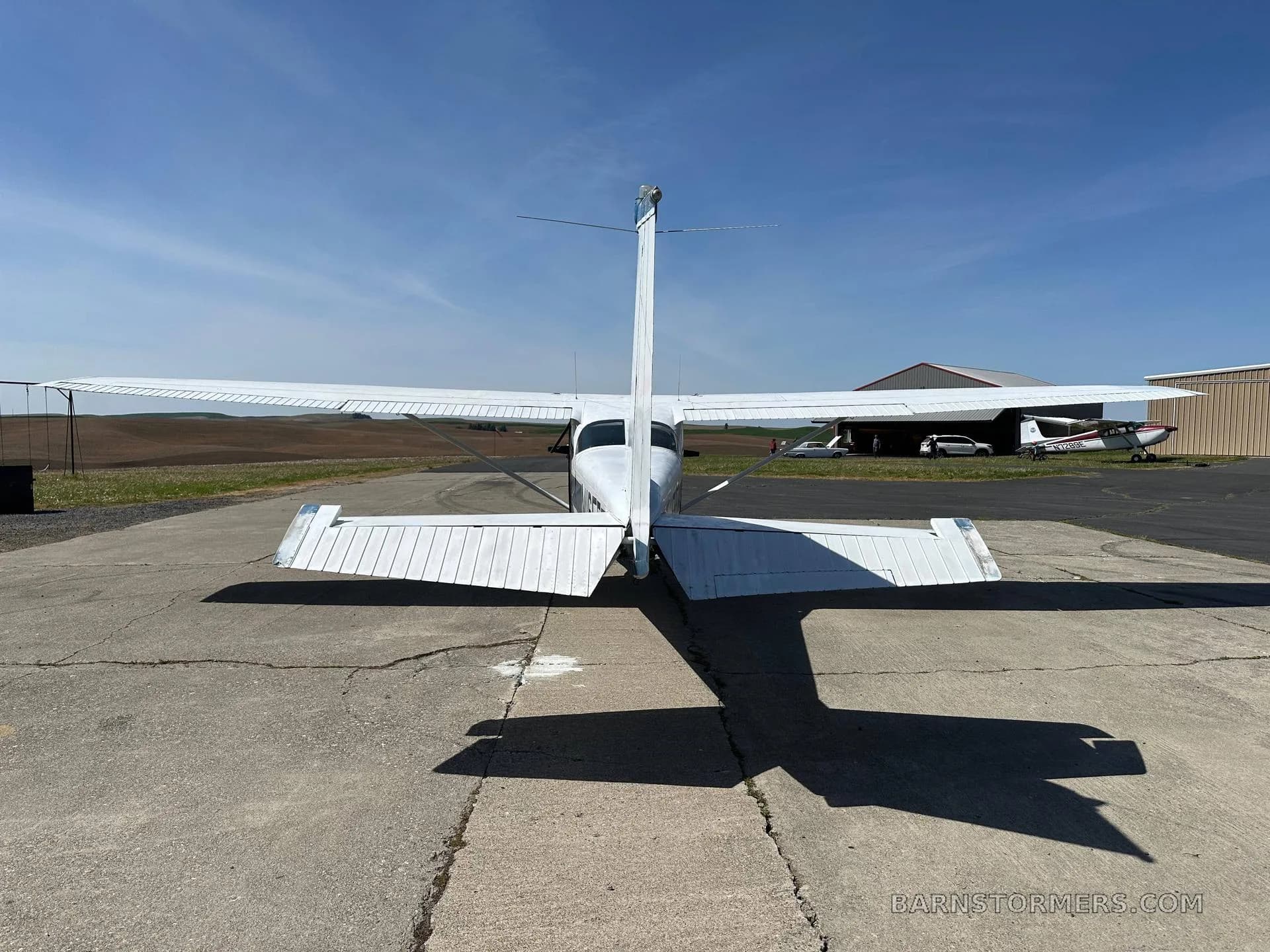 A white Cessna N1165F aircraft is viewed from the rear, showing its tail and wings on a concrete apron.