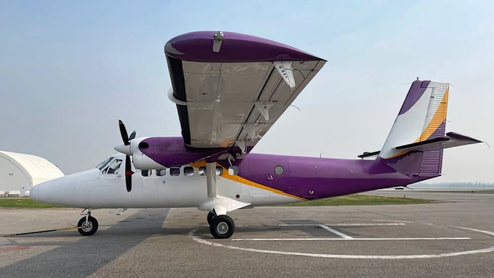 A purple and white Twin Otter aircraft parked on the tarmac.