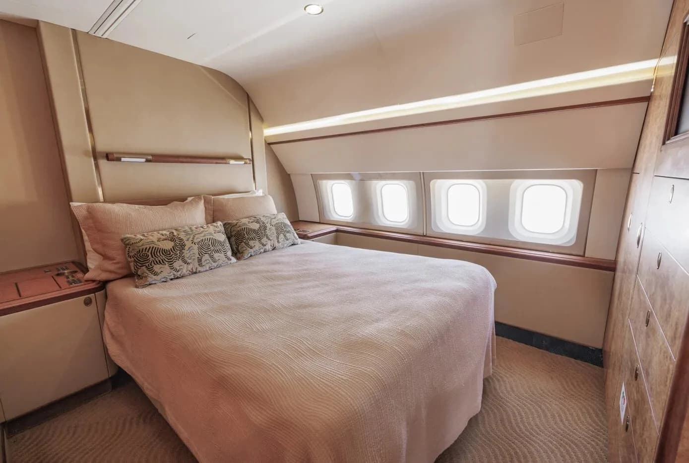 A private bedroom inside the aircraft featuring a large bed with patterned pillows and multiple windows.