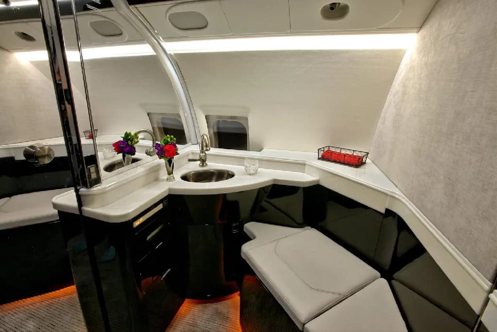 A modern galley area in the private jet cabin, featuring a sink, white countertops, and dark cabinetry.
