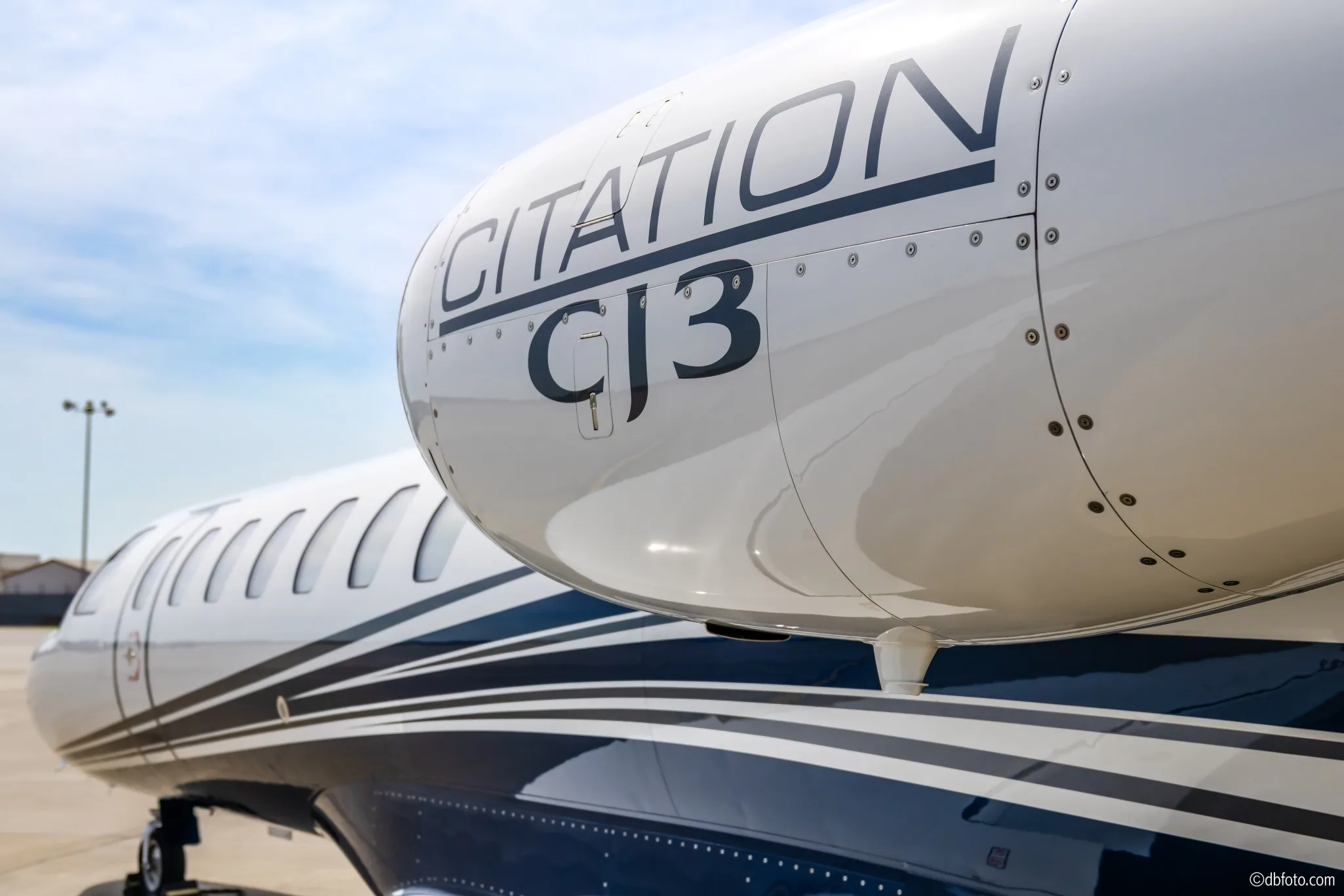 A close-up view of the "CITATION CJ3" lettering on the engine cowling of a white business jet with blue stripes.