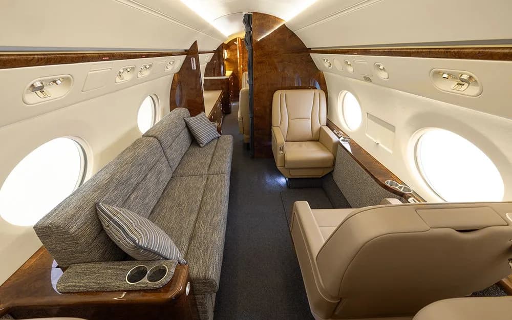 A section of the private jet cabin interior with a long sofa and a single beige leather seat.