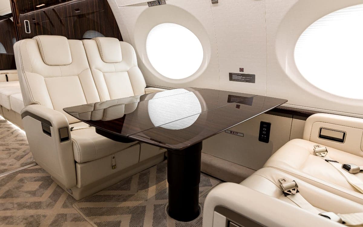 A close-up of the Gulfstream G500 cabin featuring cream-colored leather seats and a dark wood table.