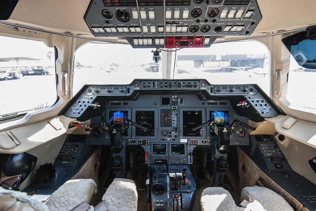 The cockpit of a business jet, showing a modern glass panel display with multiple screens and traditional controls.