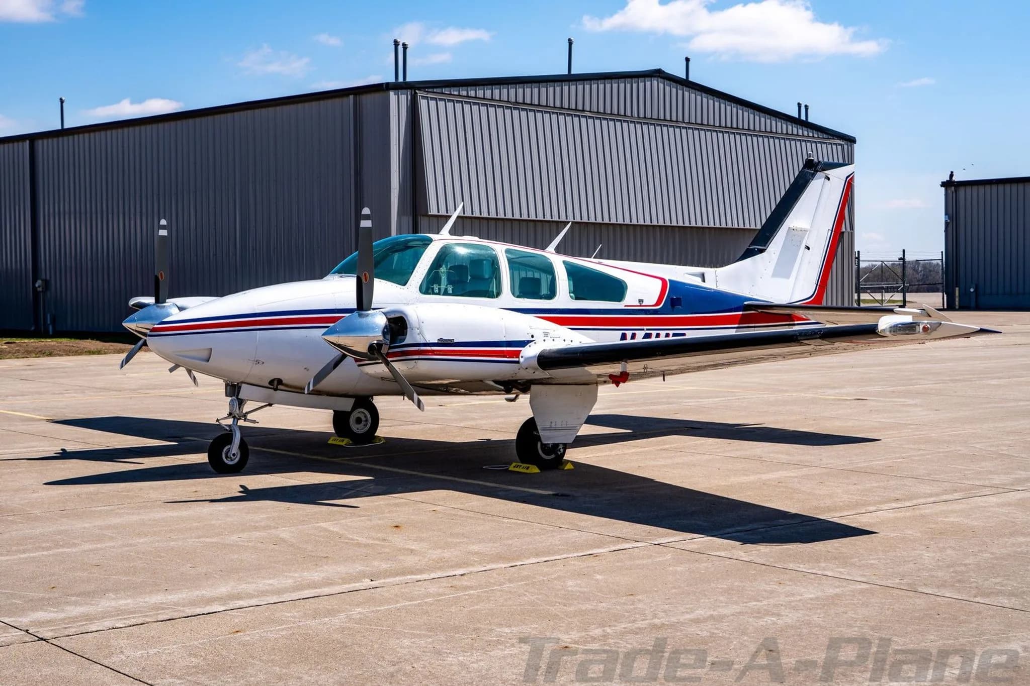 Side view of the N4UF twin-engine Beechcraft Baron with red and blue stripes parked on an airfield.