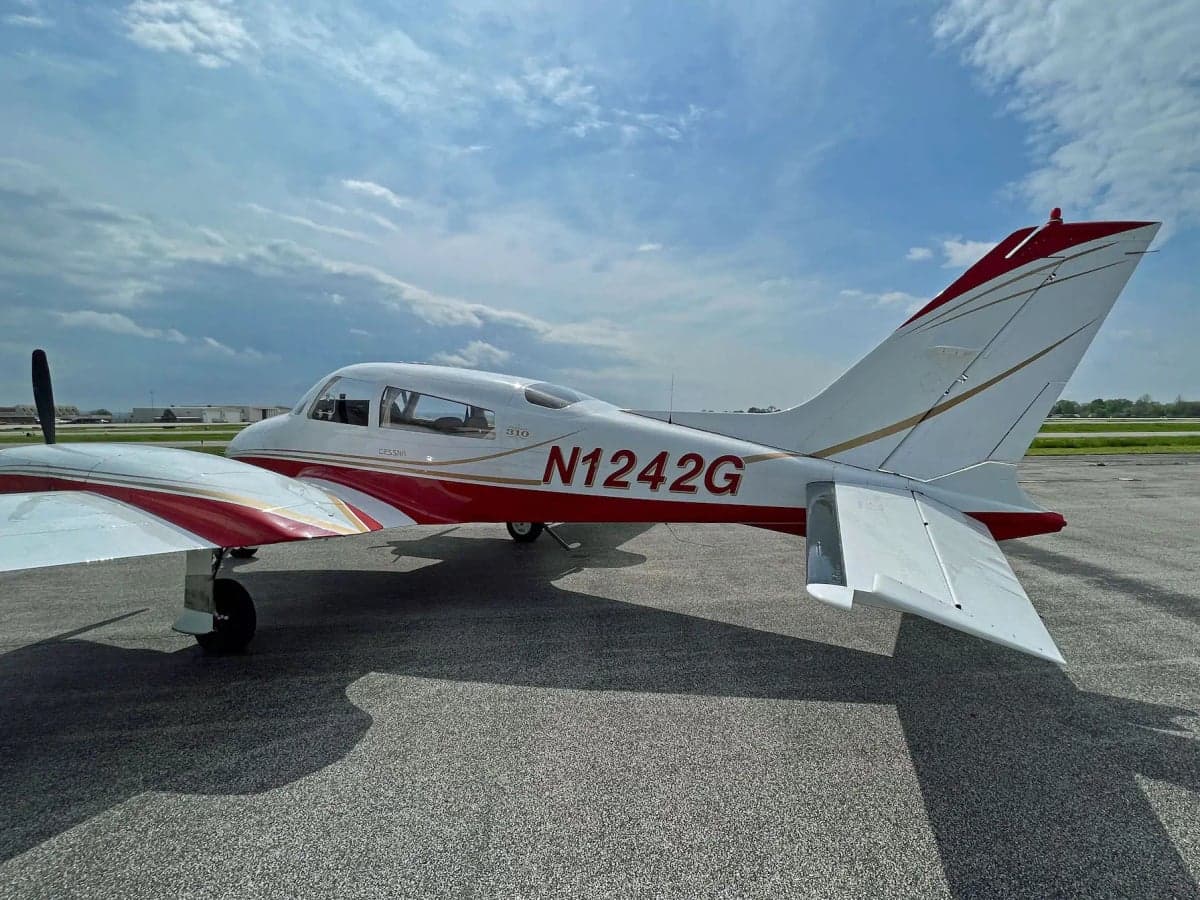 A side view of the N1242G twin-engine aircraft with red and gold stripes, parked on an airfield.