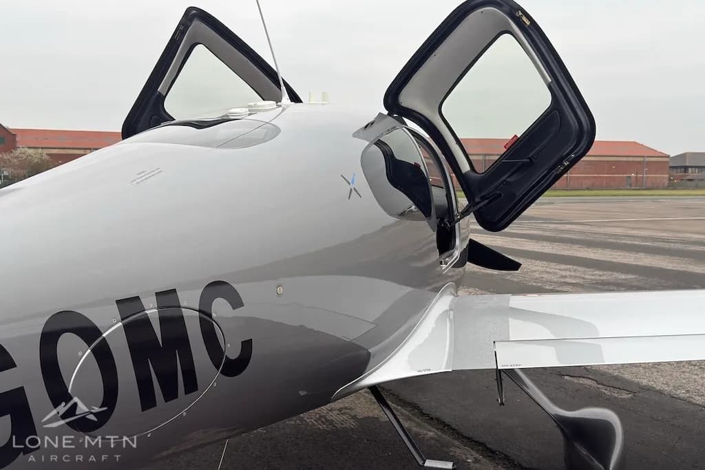 A close-up view of the front fuselage and open gull-wing doors of the silver Cirrus SR22 aircraft.