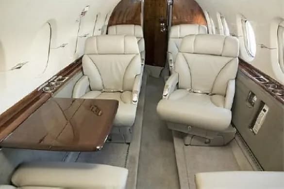 The luxurious cabin interior of a private jet with light-colored leather seats and a wooden fold-out table.