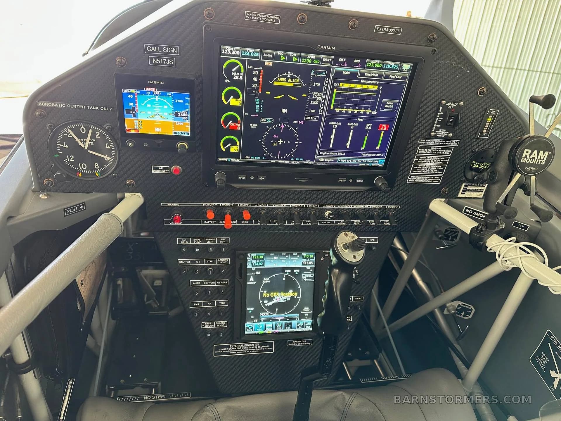 The cockpit of an Extra 300LT aircraft features a modern glass panel with Garmin displays and a carbon fiber finish.