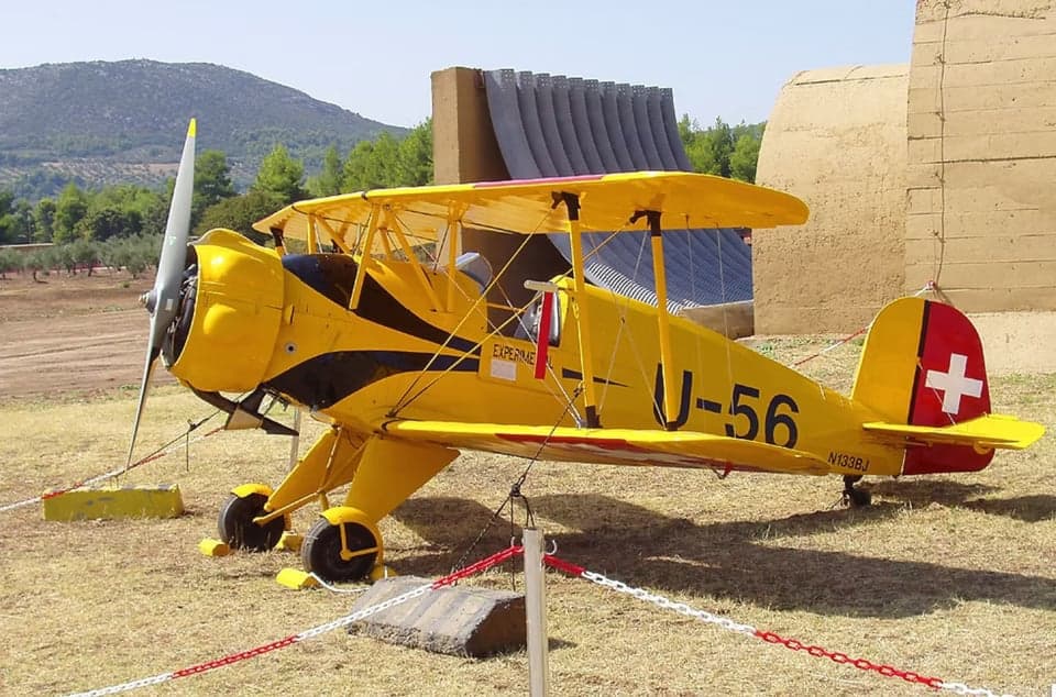 A yellow biplane with Swiss markings parked on the ground.