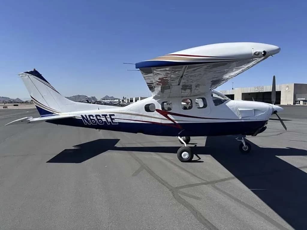 A white and blue Cessna 210 Centurion with registration N66TE parked on an airfield, showing the right side.