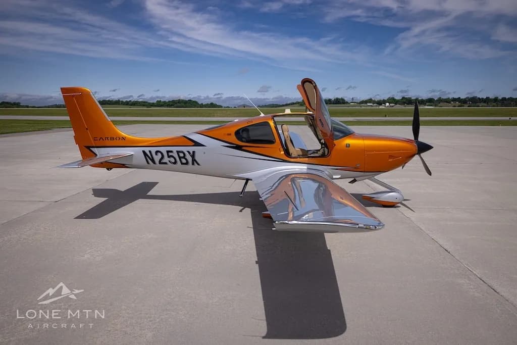 A side-right view of the orange and silver Cirrus SR22T N25BX with its doors open on an airfield.