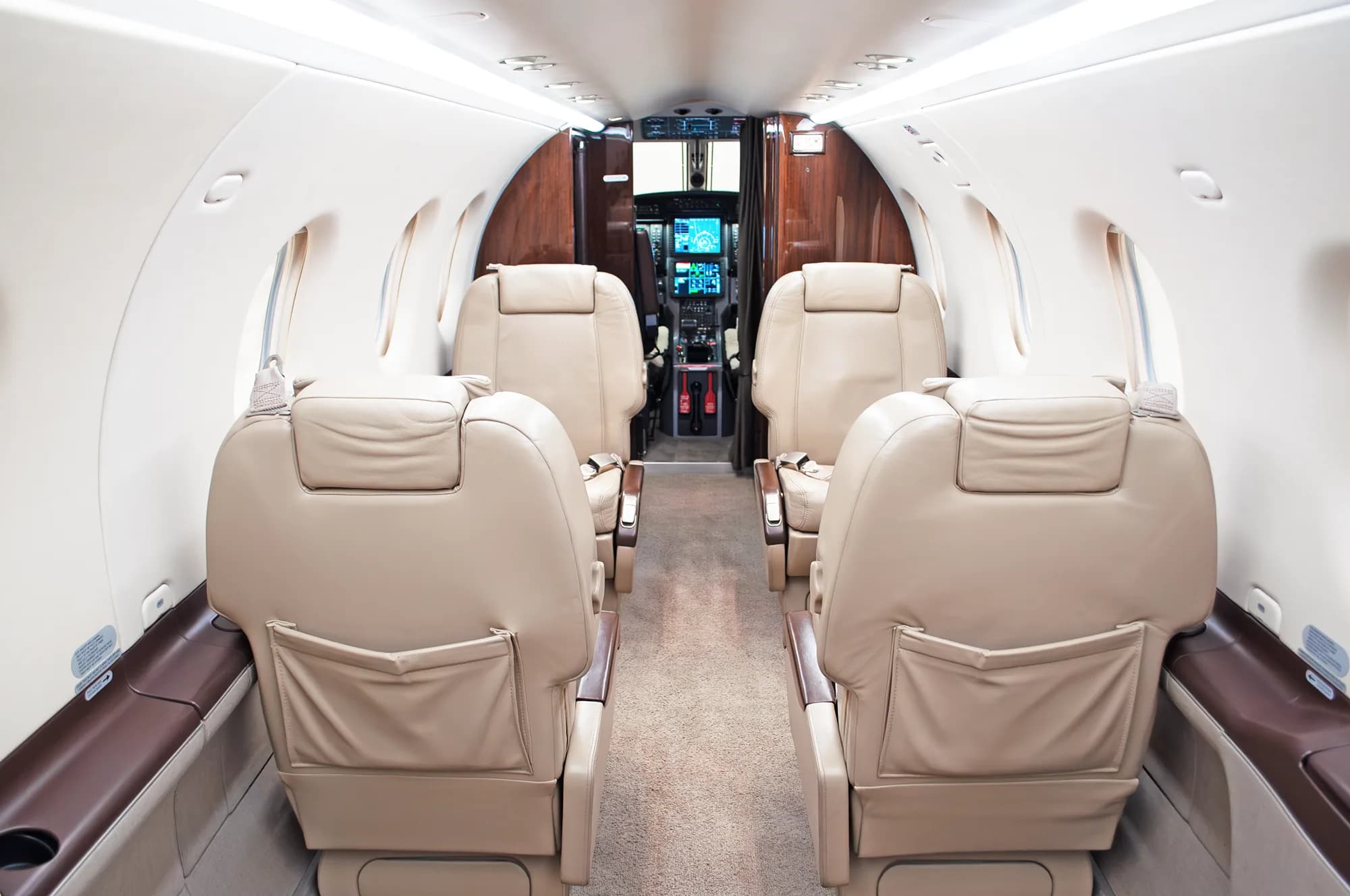 The interior cabin of a Pilatus PC-12 NG aircraft, showing beige leather seats and a view towards the cockpit.