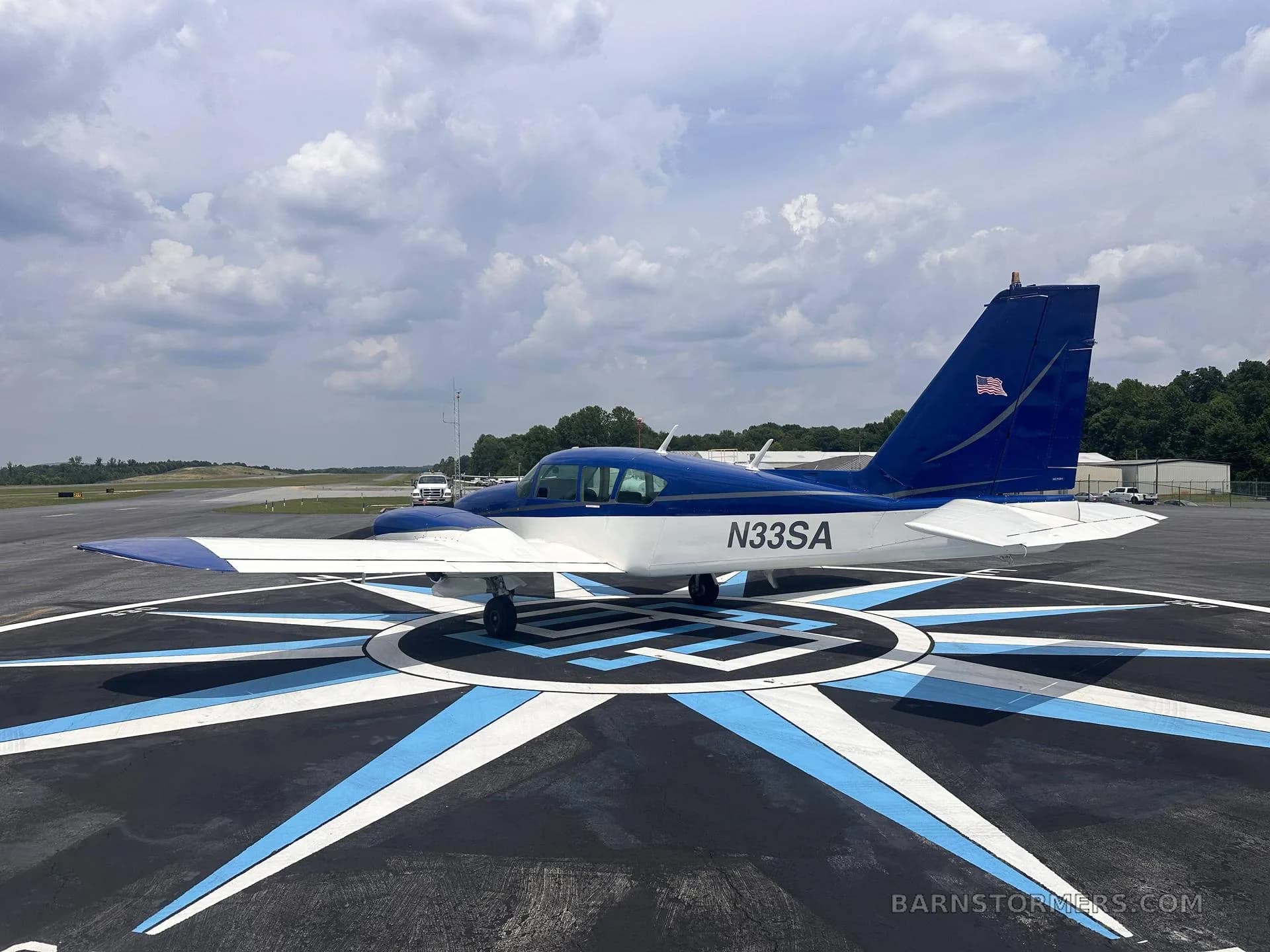 A three-quarter rear view of a blue and white single-engine aircraft (N33SA) parked on a compass rose marking on an airfield.