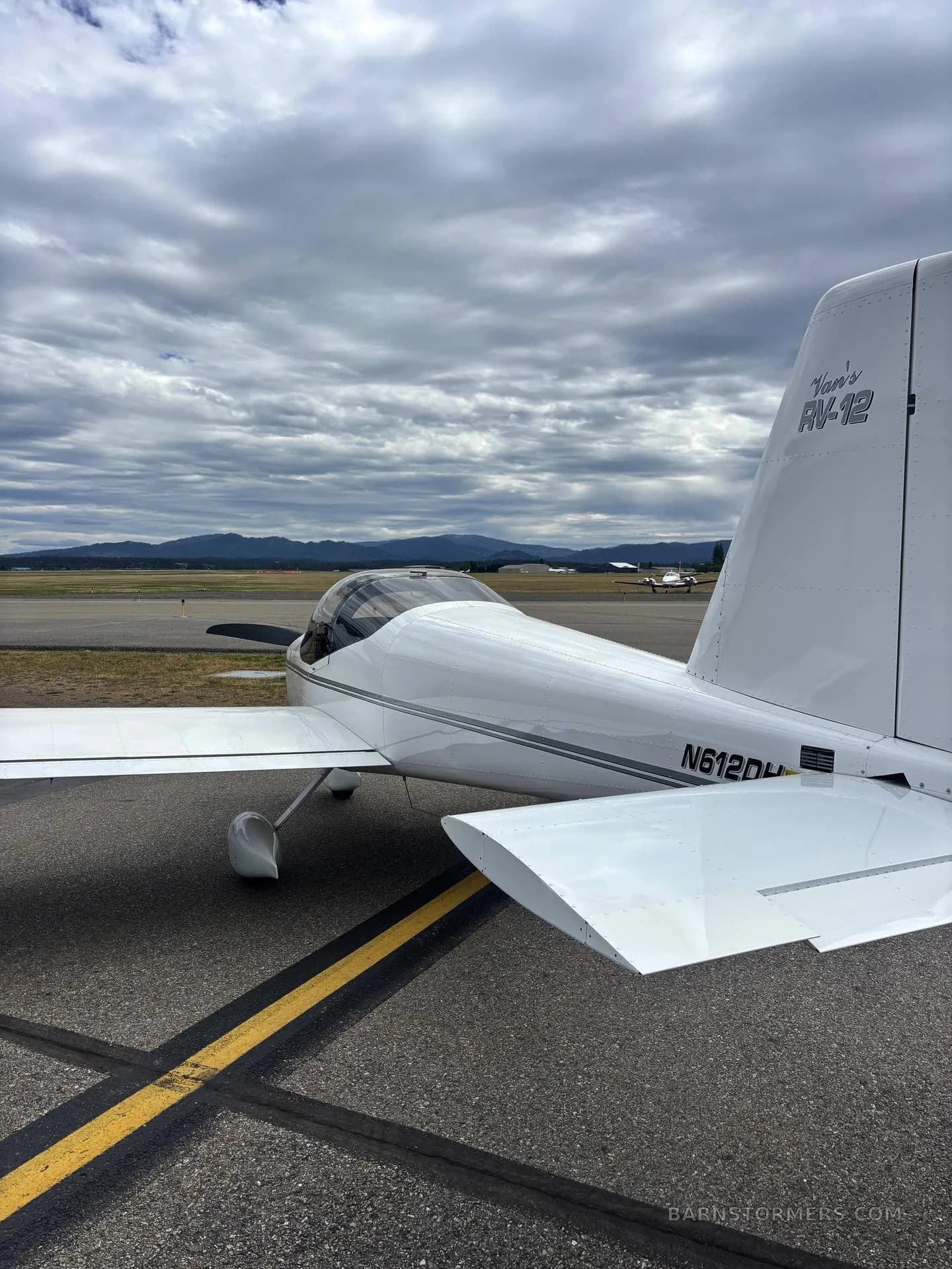 A close-up side view of the tail section of a white Vans RV-12 aircraft (N612DH) on an airfield.