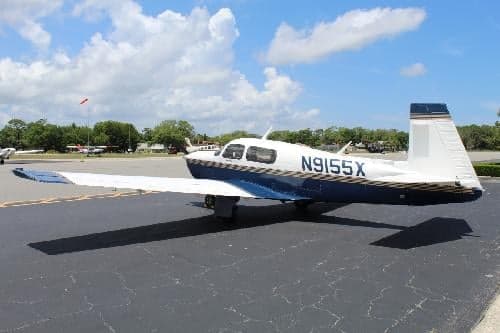 A white and blue aircraft with tail number N9155X parked on the tarmac with other aircraft in the background.