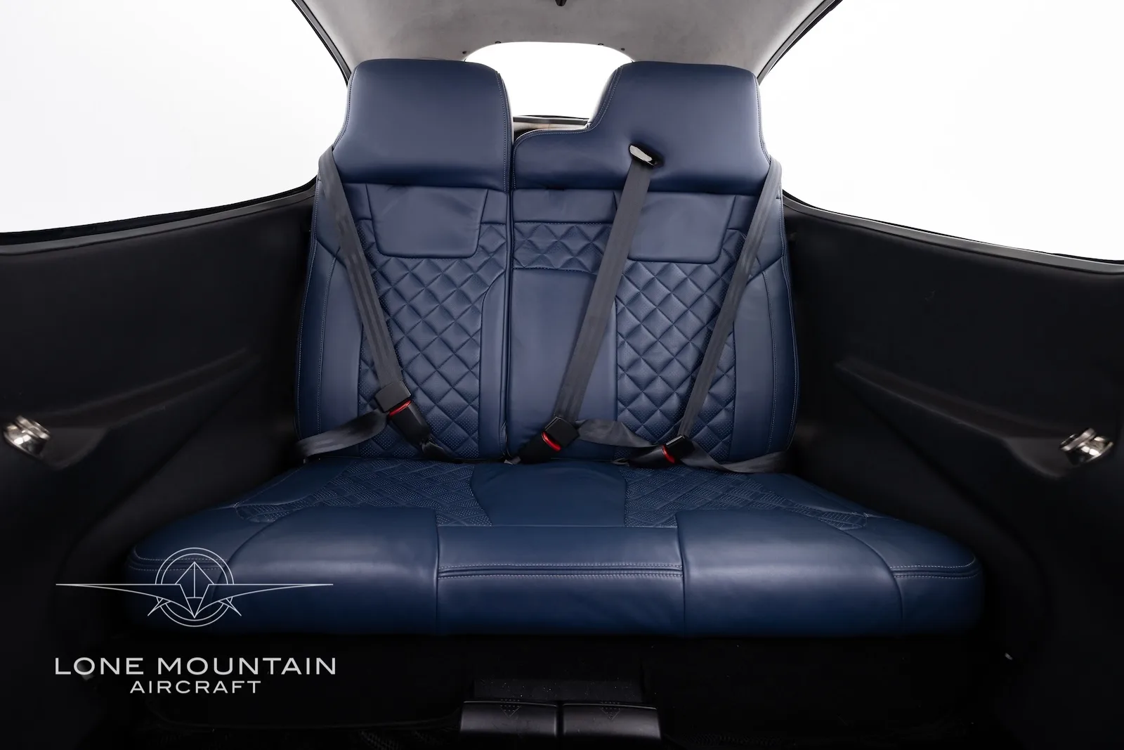 The dark blue quilted leather rear seats of an aircraft cabin.