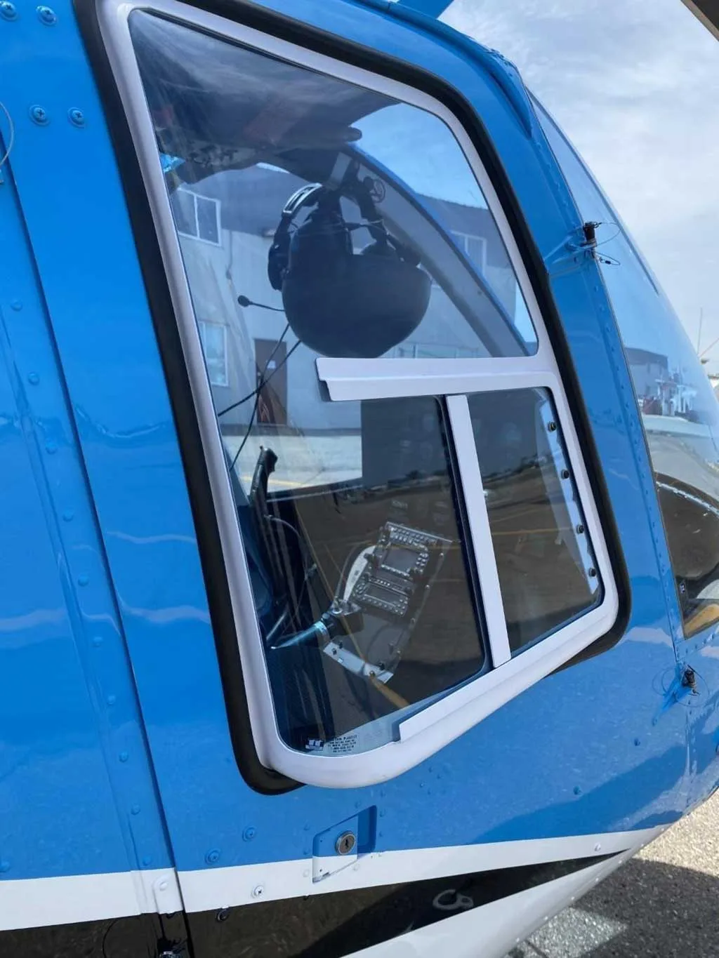 A close-up view of the cockpit window of the blue Bell 206 helicopter, N206YT, showing a headset inside.