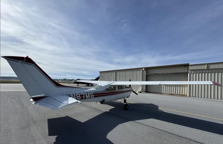 A rear-left view of a white and red Cessna 182 Skylane (N87MS) parked on an airport tarmac.
