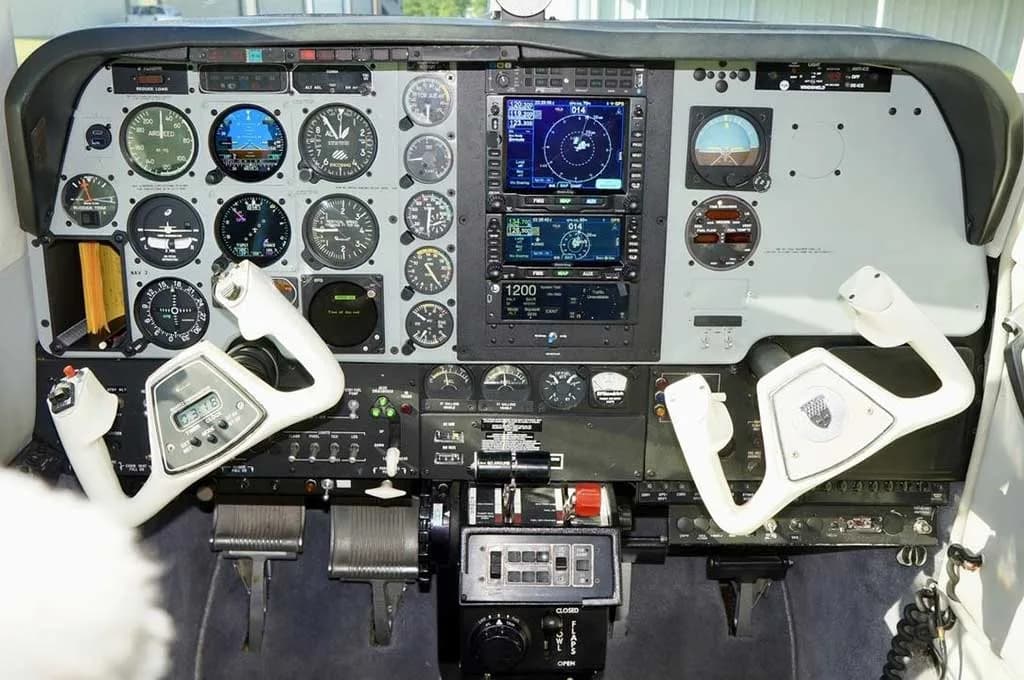 The instrument panel of a Beechcraft Baron 58 shows analog gauges, two Garmin GNS 530/430 units, and dual white yokes.