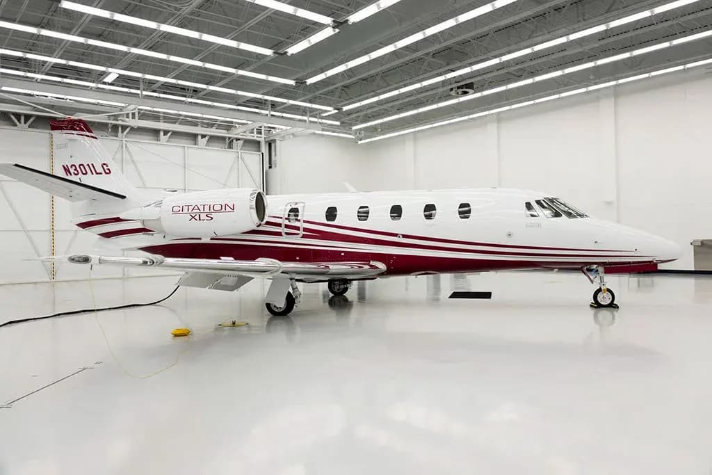 A white Cessna Citation XLS private jet with a maroon stripe and registration N301LG is parked in a brightly lit hangar, viewed from the left side.