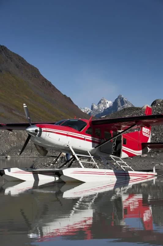 Red and white floatplane parked near a mountain.