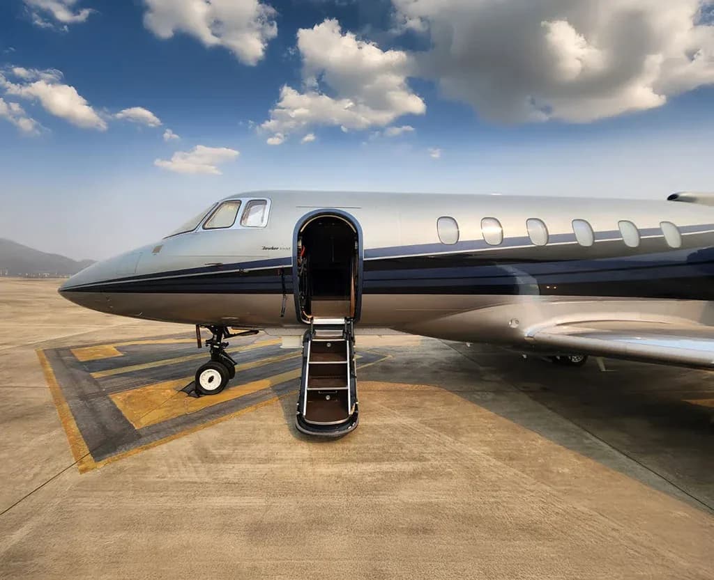 The front section of a silver and dark blue business jet with its main door open and stairs extended on an airport tarmac.