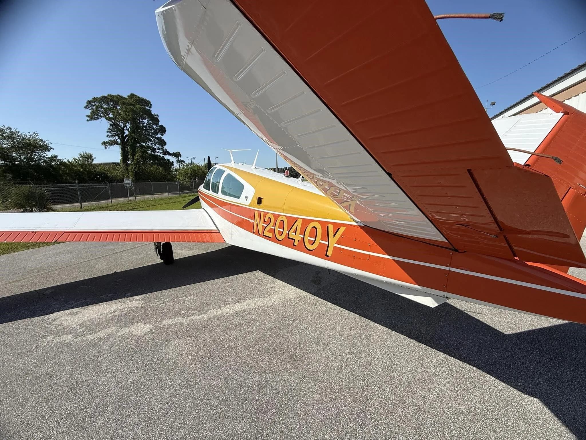 A close-up side view of the right wing and fuselage of a white and orange single-engine aircraft, N2040Y.