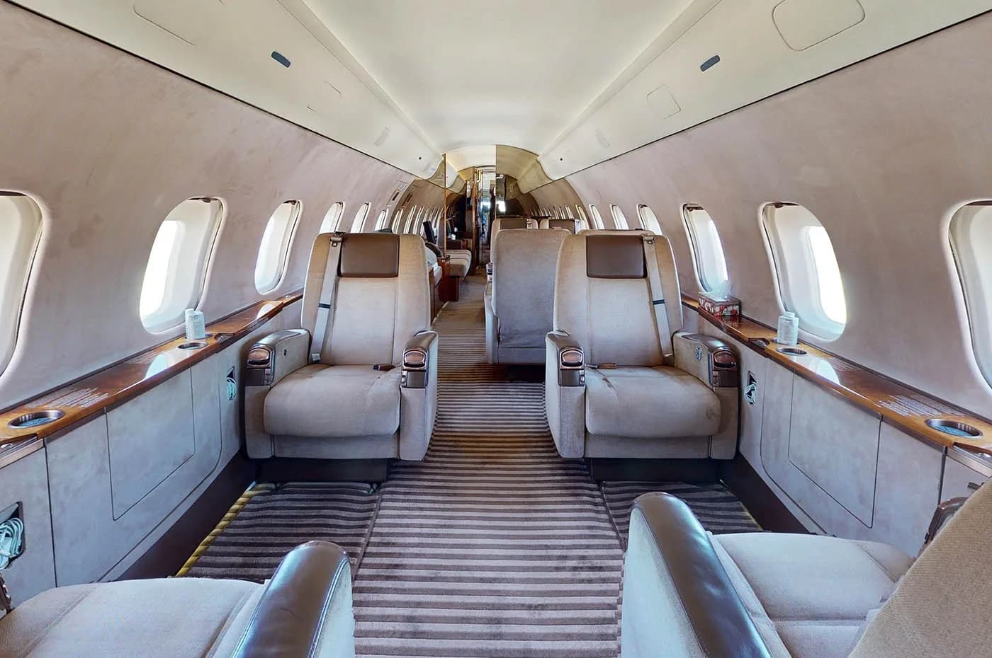 A long view down the aisle of a private jet cabin, featuring multiple rows of beige upholstered seats.
