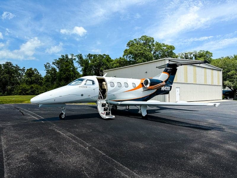 A Phenom 100 aircraft with registration N843SG is parked on the tarmac with its door open.