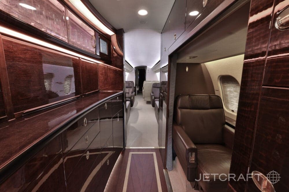 The galley area of the business jet with dark polished wood cabinetry and a view into the main cabin.