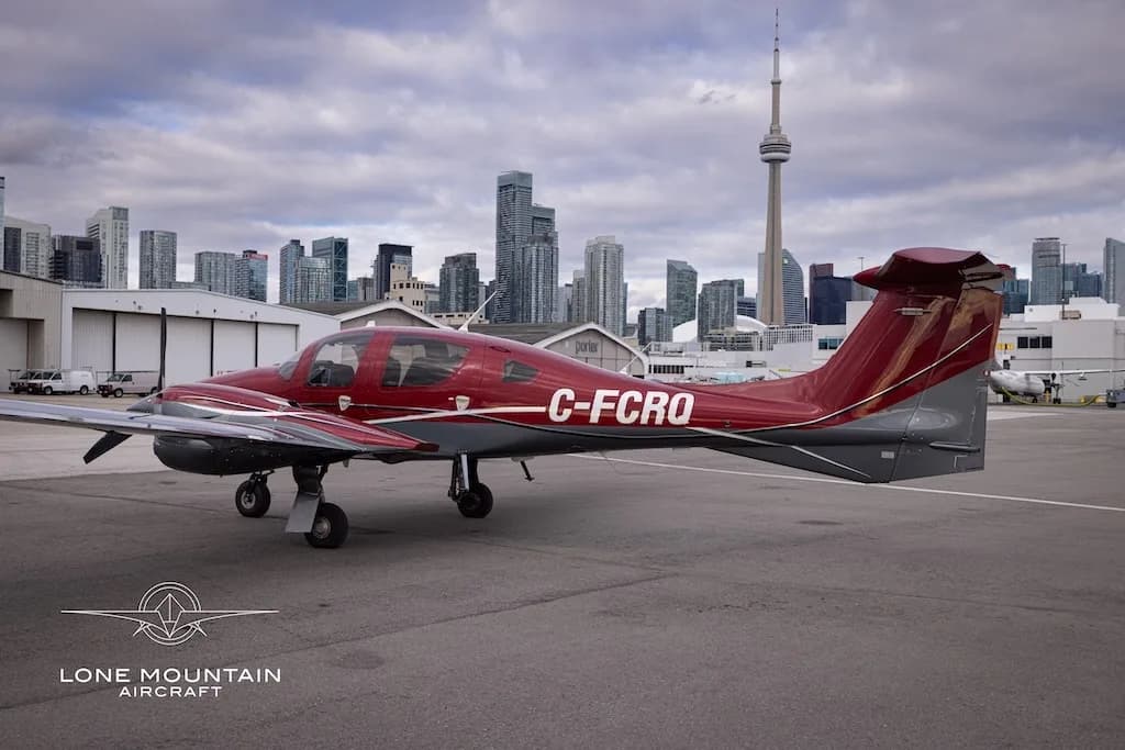A red and grey Diamond DA62 aircraft with registration C-FCRQ parked on an airfield, viewed from the side.