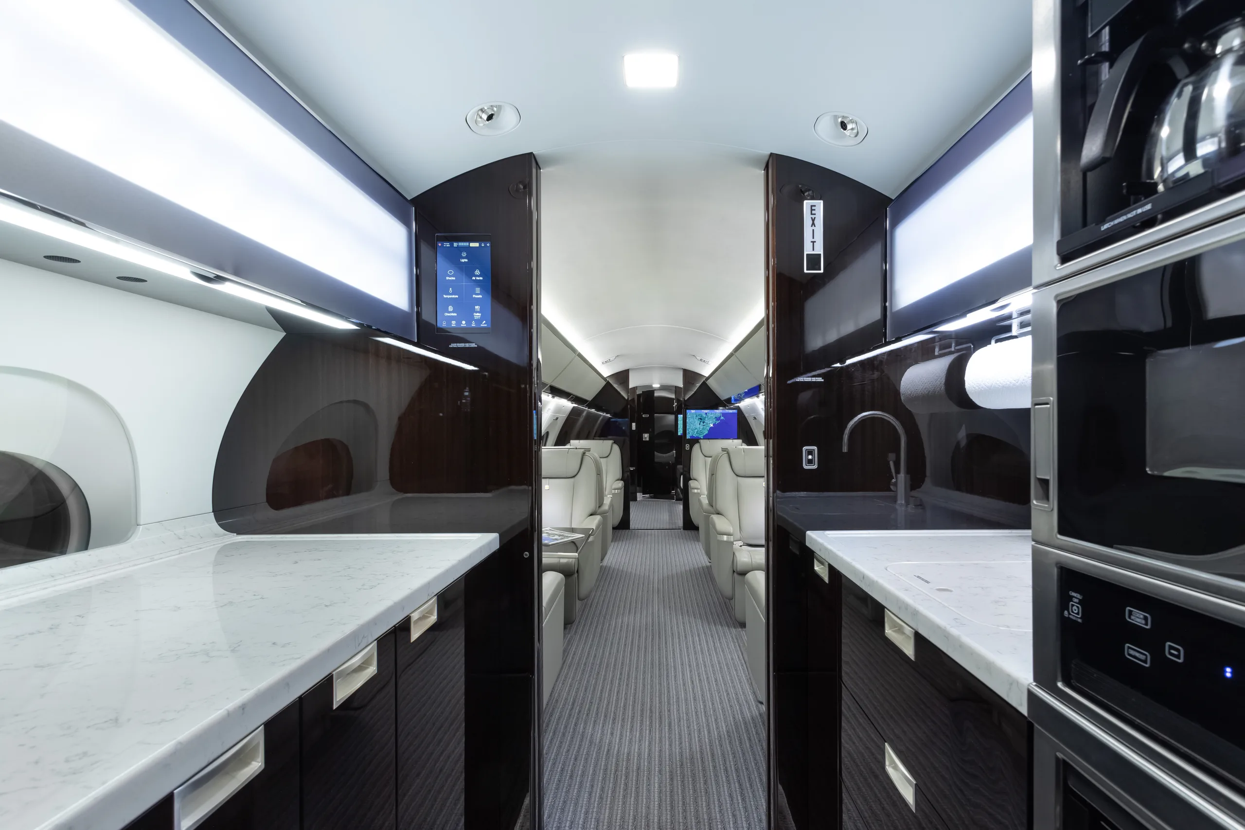 The galley of a private jet, with white marble countertops, dark wood cabinetry, a sink, and a coffee maker.
